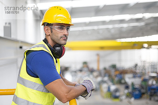 Ernste männliche Aufseher  die sich auf ein Geländer in einer Fabrik stützen