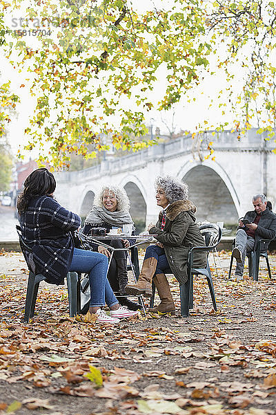 Lächelnde  aktive Seniorinnen  die im Herbst im Parkcafé Kaffee trinken