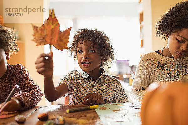 Neugieriger Junge hält Herbstblatt am Tisch