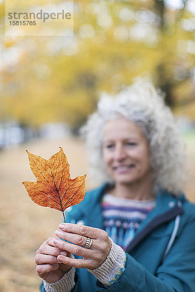Ältere Frau hält orangefarbenes Herbstblatt im Park
