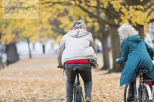 Älteres Paar fährt mit dem Fahrrad zwischen Bäumen und Blättern im Herbstpark