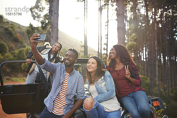 Junge Freunde mit Fotohandy machen ein Selfie von einem Jeep im Wald