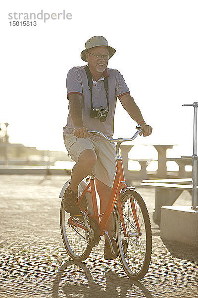Aktiver älterer Mann  der auf der sonnigen Strandpromenade Rad fährt