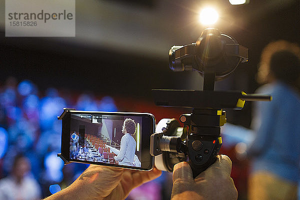 Kameramann mit Smartphone und Ausrüstung  der den Redner auf der Bühne filmt