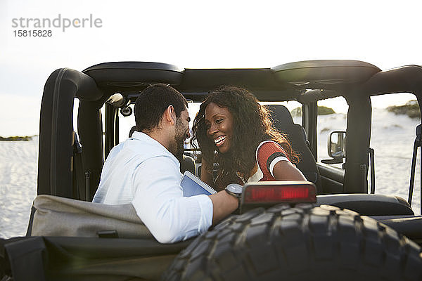 Zärtliches junges Paar lächelt auf dem Rücksitz eines Jeeps und genießt die Autofahrt