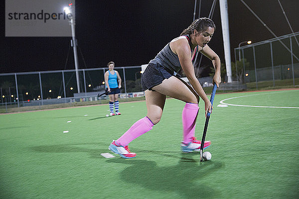 Fokussierte junge Feldhockeyspielerin  die nachts auf dem Feld spielt