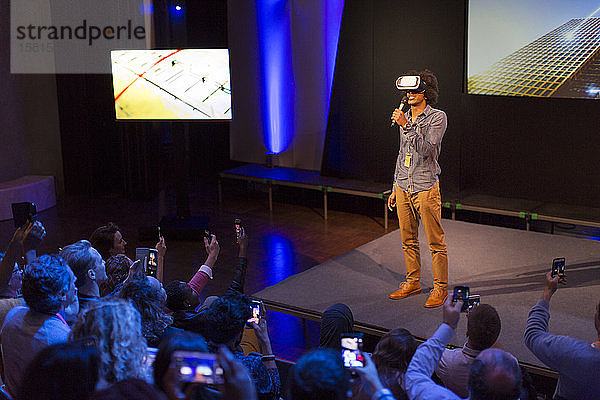 Publikum beobachtet männlichen Redner mit Virtual-Reality-Simulatorbrille auf der Bühne