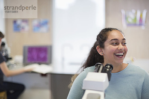 Lachende Studentin am Mikroskop im Laborunterrichtsraum