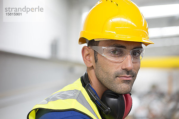 Porträt ernsthafter männlicher Arbeiter mit Schutzbrille und Schutzhelm in einer Fabrik