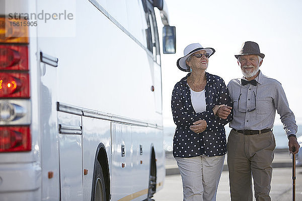 Lächelndes aktives Seniorenpaar  das am Bus entlang spaziert