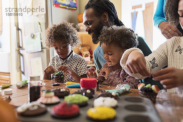 Familie dekoriert Halloween-Cupcakes am Tisch