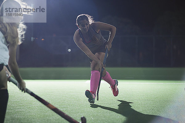 Entschlossene junge Feldhockeyspielerin  die mit einem Hockeyschläger läuft und nachts auf einem Feld spielt