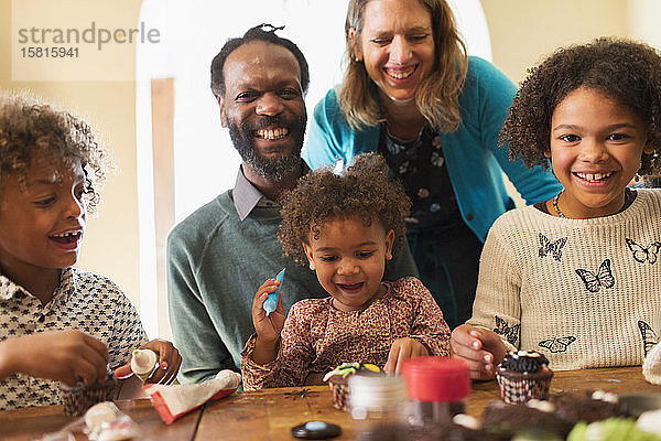 Porträt einer glücklichen multiethnischen Familie  die am Tisch Törtchen verziert