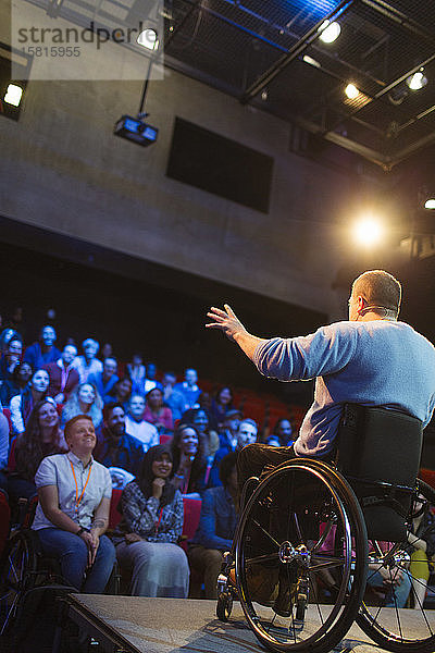 Publikum beobachtet männlichen Redner im Rollstuhl  der auf der Bühne spricht