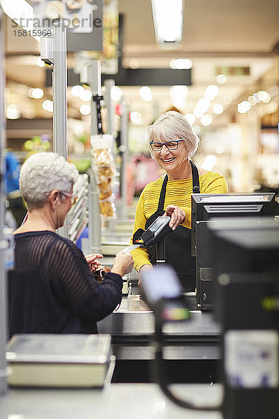 Ältere weibliche Kassiererin hilft Kunden an der Supermarktkasse