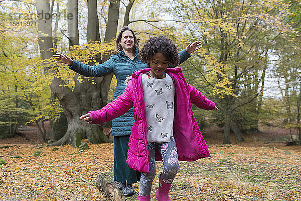 Mutter und Tochter balancieren auf einem umgestürzten Baumstamm im Herbstwald