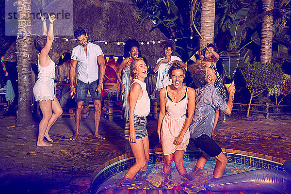 Begeisterte junge Freunde tanzen und hängen bei einer nächtlichen Sommerparty am Pool herum