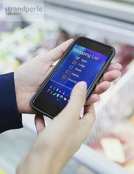 Nahaufnahme einer Frau  die eine digitale Einkaufsliste auf einem Smartphone im Supermarkt benutzt