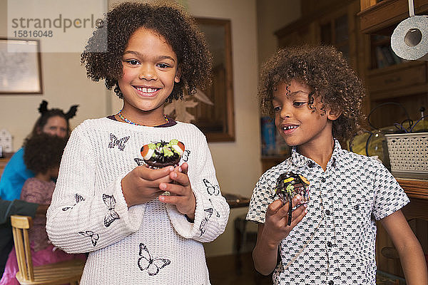 Portrait glückliche Geschwister mit dekorierten Halloween-Cupcakes