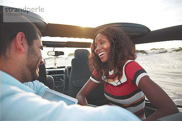 Lächelndes junges Paar auf dem Rücksitz eines Jeeps am Strand  das einen Roadtrip genießt