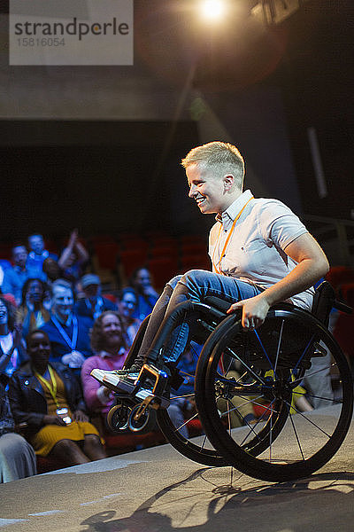Lächelnde Sprecherin  die auf der Bühne einen Wheelie im Rollstuhl macht