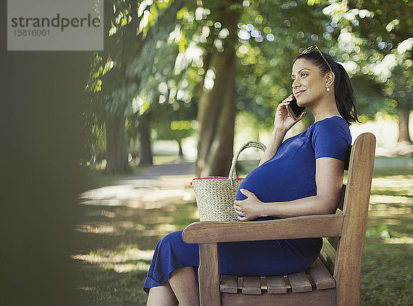 Schwangere Frau spricht auf einer Parkbank mit ihrem Handy