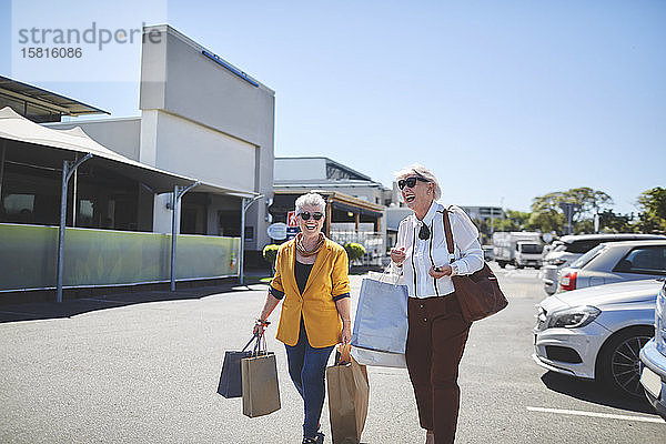 Glückliche ältere Frauen mit Einkaufstaschen auf einem sonnigen Parkplatz