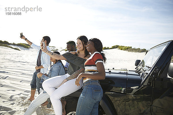 Junge Freunde mit Kameratelefonen machen ein Selfie am Jeep am sonnigen Strand