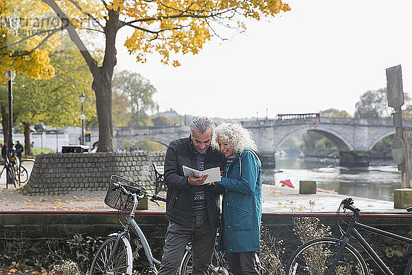 Älteres Ehepaar mit Fahrrädern unterwegs  Blick in einen Reiseführer entlang eines herbstlichen Flusses