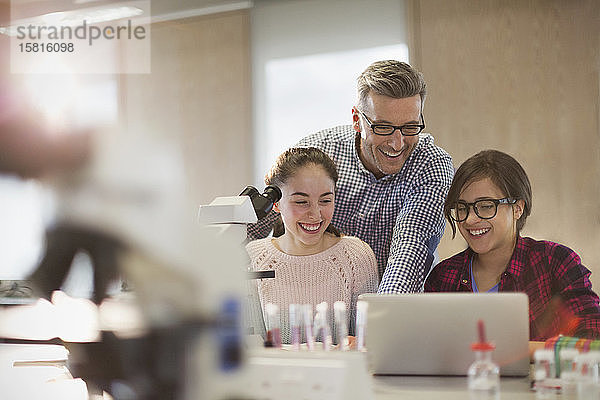 Männlicher Lehrer und weibliche Schüler  die ein wissenschaftliches Experiment an einem Mikroskop und einem Laptop in einem Laborklassenzimmer durchführen