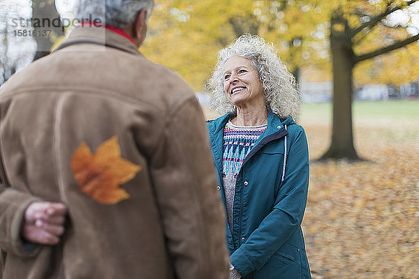 Verspielter älterer Ehemann überrascht Frau mit Herbstblatt im Park