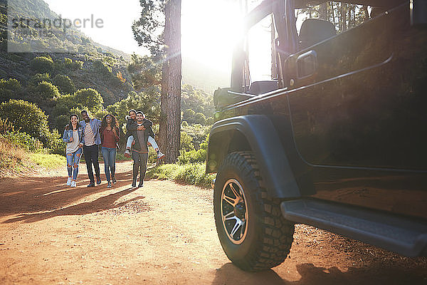 Junge Freunde gehen auf einem sonnigen Feldweg im Wald auf einen Jeep zu