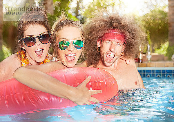 Porträt ausgelassener  verspielter junger Freunde mit aufblasbarem Floß im Sommerschwimmbad