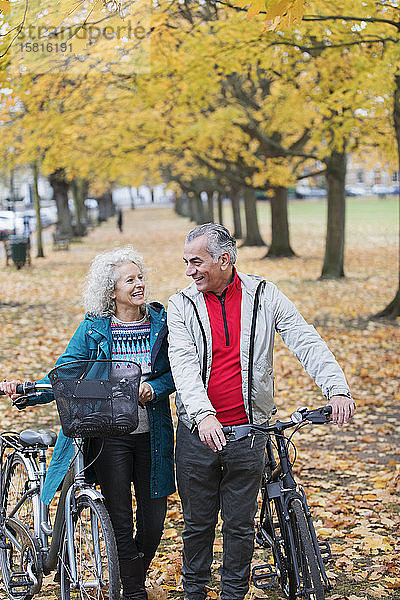 Älteres Paar  das zwischen Bäumen und Blättern im Herbstpark Fahrrad fährt
