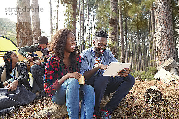 Lächelndes junges Paar  das auf einem Campingplatz im Wald ein digitales Tablet benutzt