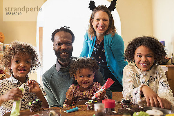Porträt einer glücklichen Familie  die Halloween-Cupcakes am Tisch dekoriert