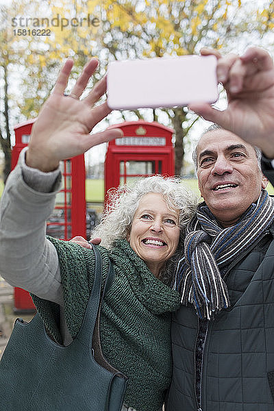 Lächelndes älteres Paar  das ein Selfie im Park vor einer roten Telefonzelle macht
