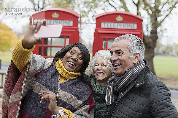 Ältere Freunde machen ein Selfie vor einer roten Telefonzelle im Herbstpark