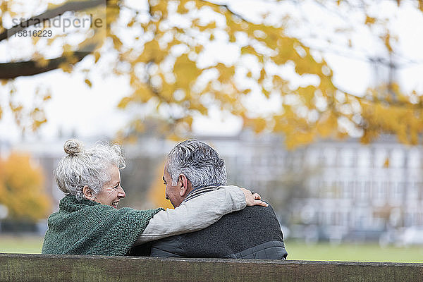 Unbeschwertes  zärtliches älteres Paar  das sich auf einer Bank im Herbstpark umarmt