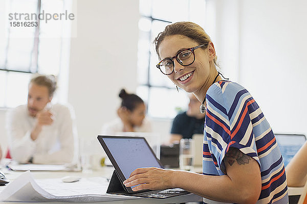 Porträt einer lächelnden  selbstbewussten Architektin  die in einem Konferenzraum an einem Laptop arbeitet