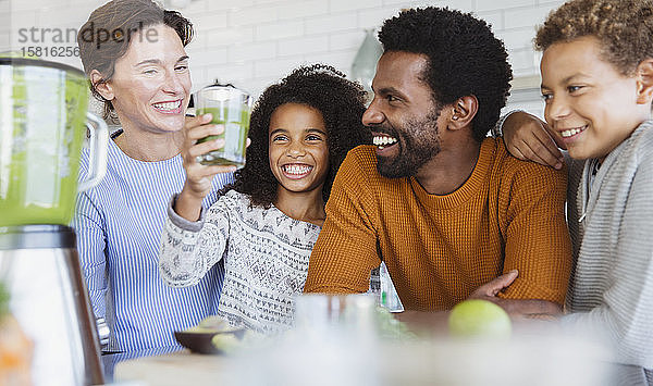 Lächelnde multiethnische Familie trinkt gesunden grünen Smoothie in der Küche