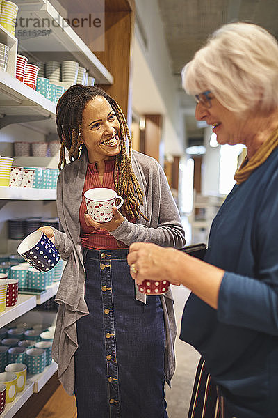 Lächelnde Mitarbeiterin hilft einer älteren Frau beim Einkaufen von Tassen