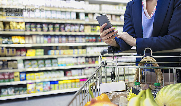 Frau mit Smartphone beim Einkaufen im Supermarkt