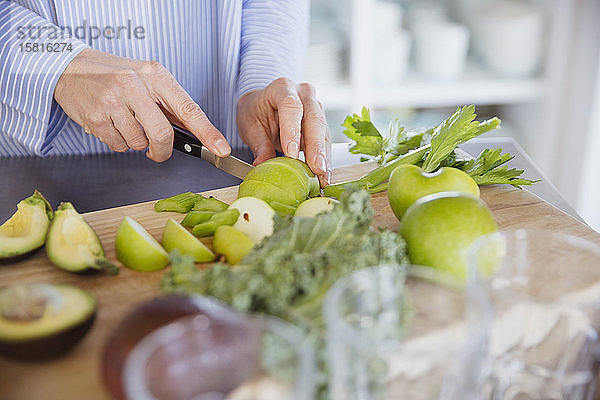 Frau schneidet gesunde grüne Äpfel und Gemüse auf einem Schneidebrett