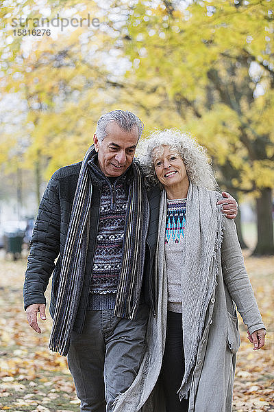 Selbstbewusstes  lächelndes älteres Paar  das sich umarmt und im Herbstpark spazieren geht