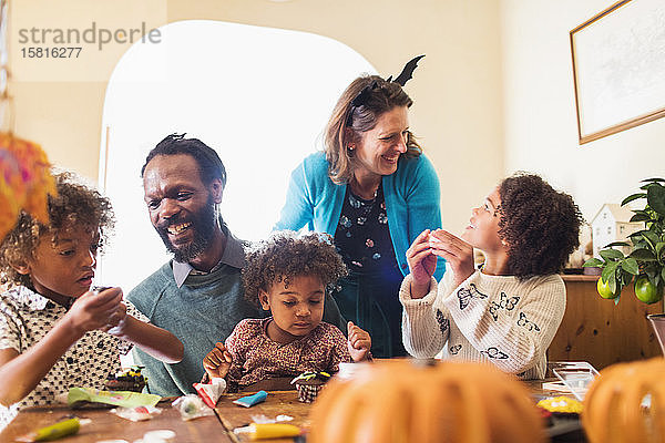 Glückliche Familie dekoriert Halloween-Cupcakes am Tisch