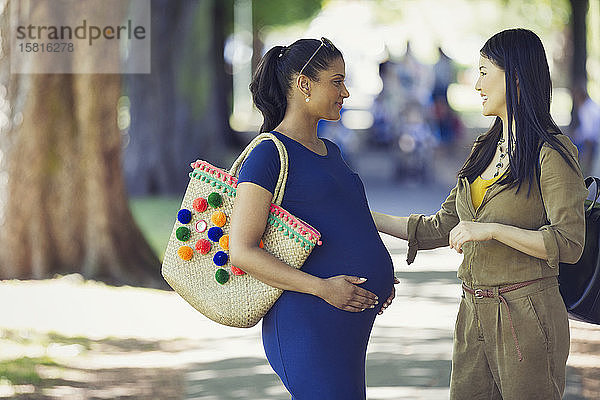 Frau begrüßt schwangere Freundin im Park
