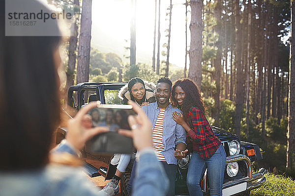 Junge Frau mit Fotohandy fotografiert Freunde im Jeep im Wald