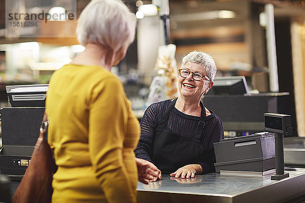 Glückliche ältere weibliche Kassiererin  die Kunden an der Supermarktkasse begrüßt