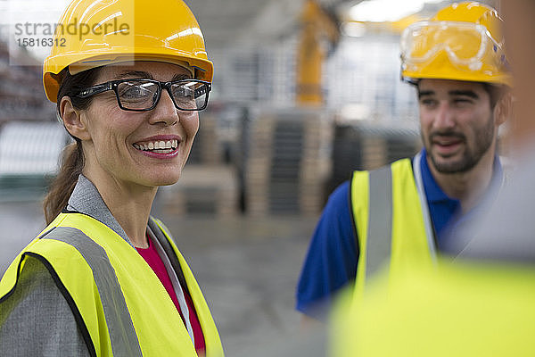 Lächelnde Arbeiterin im Gespräch mit Arbeitskollegen in einer Fabrik